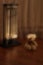 A soft toy bear is basking near an old electric heater on the floor