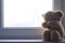A soft toy bear cries sitting on a windowsill. There are noises in the photo, because the photo
