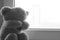 A soft toy bear cries sitting on a windowsill. There are noises in the photo, because the photo is dark.