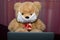 Soft toy, bear, in a protective gauze mask. Sits at a laptop. Symbol of self-isolation during a virus outbreak