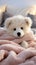 A soft white teddy bear sits atop a cozy merino blanket on a bed