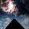 Solar eclipse shining through the clouds in the sky above a pyramid