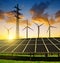 Solar panels with wind turbines and electricity pylon at sunset.