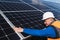 Solar power plant worker in hard hat checks the surface of the photovoltaic panel with his hand for damage.