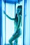 Solarium. Pretty girl with african braids in a dress for oriental dances sunbathing in a vertical sunbed. Blue neon glow