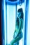 Solarium. Pretty girl with african braids in a dress for oriental dances sunbathing in a vertical sunbed. Blue neon glow