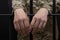 Soldier in military uniform behind bars against a black background. Concept: court martial, refusal to mobilize, crime in the army