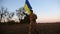 Soldier of ukrainian army running with raised blue-yellow banner on field at dusk. Young male military in uniform