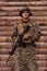 A soldier in uniform with a rifle in his hand is standing in front of a wooden wall. A soldier guards the forest base