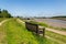 A solitary bench on the bank of a river with a clear view down river and of the nearby boatyard. A place to think and think