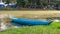 Solitary Blue Boat: A lone blue boat rests by the green bank of a meandering muddy river