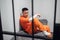 Solitary cell with a criminal in an orange robe in an asian prison. Copy space. Sad emotions of a young guy.