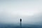 Solitary figure standing in a foggy expanse. Conceptual minimalist photography with a sense of solitude and