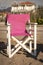 A solitary pink canvas chair sits abandoned on a serene Greek beach, bathed in the golden light of the setting sun, offering a