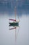 A solitary sailboat sits on calm water with a clear reflection.