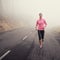 The solitude of an early jog. A young woman jogging on a country road on a misty morning.