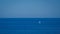 Solitude takes center stage as a lone sailing boat charts its course through the calm embrace of clear, azure waters.