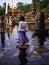 Solo Female Traveler Walking on Stepping Stones around Koi Fish at Main fountain at Tirta Gangga, Bali