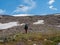 Solo hiking in the mountains. A man climbs a mountain slope. In the background is a dome of snow-capped mountains under a blue sky