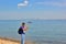 Solo traveling man with backpack standing on the pebble beach with sea and city background