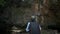 Solo woman adventurer is walking into the cave under steep cliff that covering by green plants during summer.