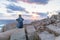 Solo young female traveler watches a beautiful sunset on spectacular rocks of Capo Testa, Sardinia, Italy.