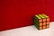 Solved puzzle speed cube on white wooden shelf near red colored wall, colorful rubiks cube with copy space mind challanging