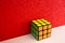 Solved puzzle speed cube on white wooden shelf near red colored wall, colorful rubiks cube with copy space mind challanging