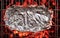 Some food in aluminum foil on  grate over hot pieces of coals. Top view