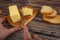 Someone cuts off some butter with a knife from a piece in a wooden butter dish, slices of cheese and fresh wheat toast on a wooden