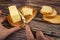 Someone cuts some butter with a knife from a piece of butter in a wooden butter dish, slices of cheese and fresh wheat toast on a