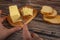 Someone cuts some butter from a piece in a wooden butter dish, slices of cheese and fresh wheat toast on a wooden background.