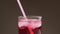 Someone drinking red soda water with ice from the glass throw the straw