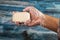 Someone is holding a piece of toilet soap on a wooden background in a soapy hand. Frequent hand washing with soap is a prevention