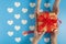 Someone sending the brown gift box tied with red ribbon over the blue background with white heart