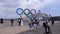 Someone takes pictures next to the five ring symbol of the Olympic Games at red brick warehouse in the background a large cruise