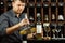 Sommelier decants white wine in decanter over cellar of bottle background