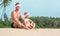 Son and Father dressed santa hats sit together on sandy tropical