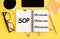 SOP - Standard Operating Procedure, text on notepad and office accessories on yellow desk