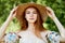 A sophisticated red-haired girl in a simple linen dress, in a light wide-brimmed hat.Model look. Natural beauty