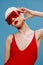 A sophisticated red-lipped lady in a swimming cap and a red swimsuit touches her glasses and looks aside posing on a