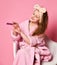 Sophisticated young lady teen girl in bathrobe sits in fashion designer armchair and makes manicure with nail file on pink