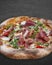 Sorrentina pizza with prosciutto, arugula, capers, pelati sauce, pesto. Neapolitan round pizza on dark background