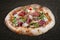 Sorrentina pizza with prosciutto, arugula, capers, pelati sauce, pesto. Neapolitan round pizza on wood background