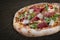 Sorrentina pizza with prosciutto, arugula, capers, pelati sauce, pesto. Neapolitan round pizza on wood background