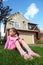 Sorrowful girl sits on grass near cottage