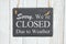 Sorry we`re Closed Due to weather text on a hanging chalkboard on weathered whitewash textured wood