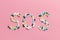 SOS sign made of pills and capsules on a pink background. The concept of illness and drug addiction. Suicide. Death from