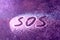 SOS word hand written on white powder, distress signal