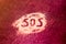 SOS word hand written on white powder, distress signal